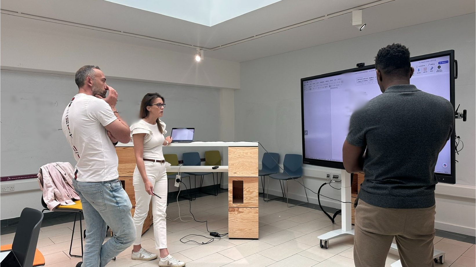 A small group session in a skylit room — two clients working alongside John at the shared screen