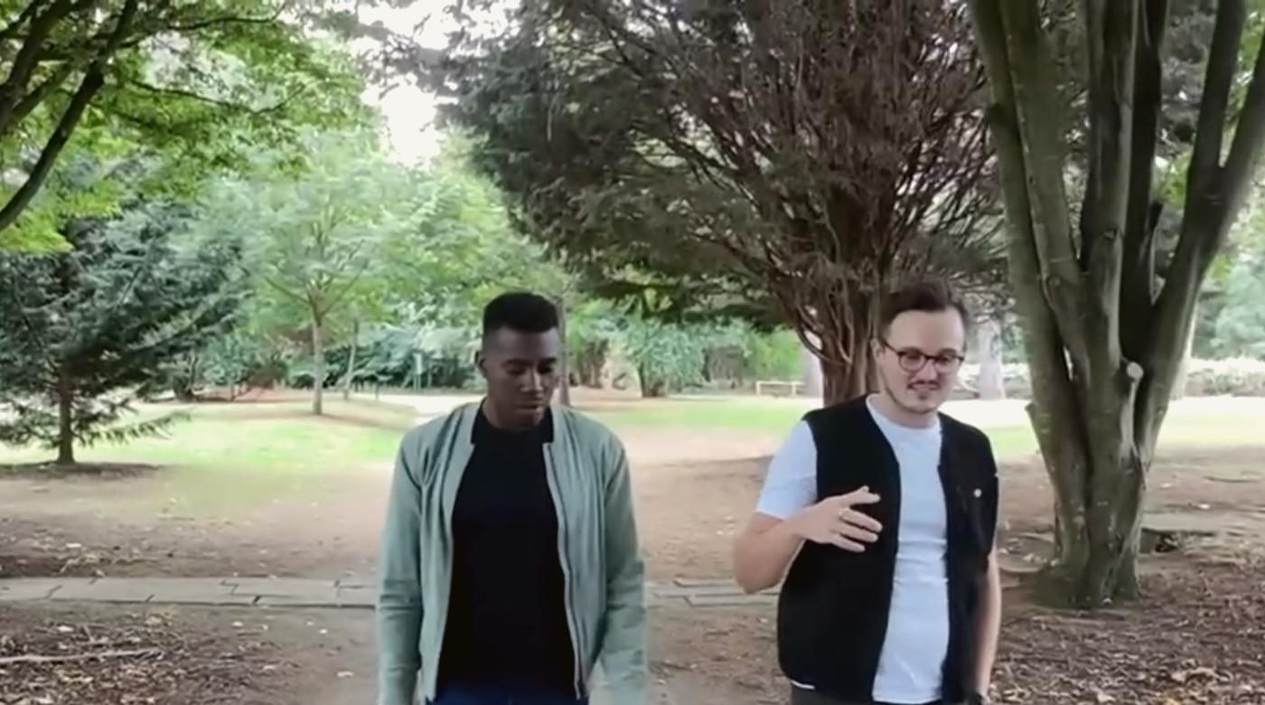 Two men walking a wooded path, mid-conversation.